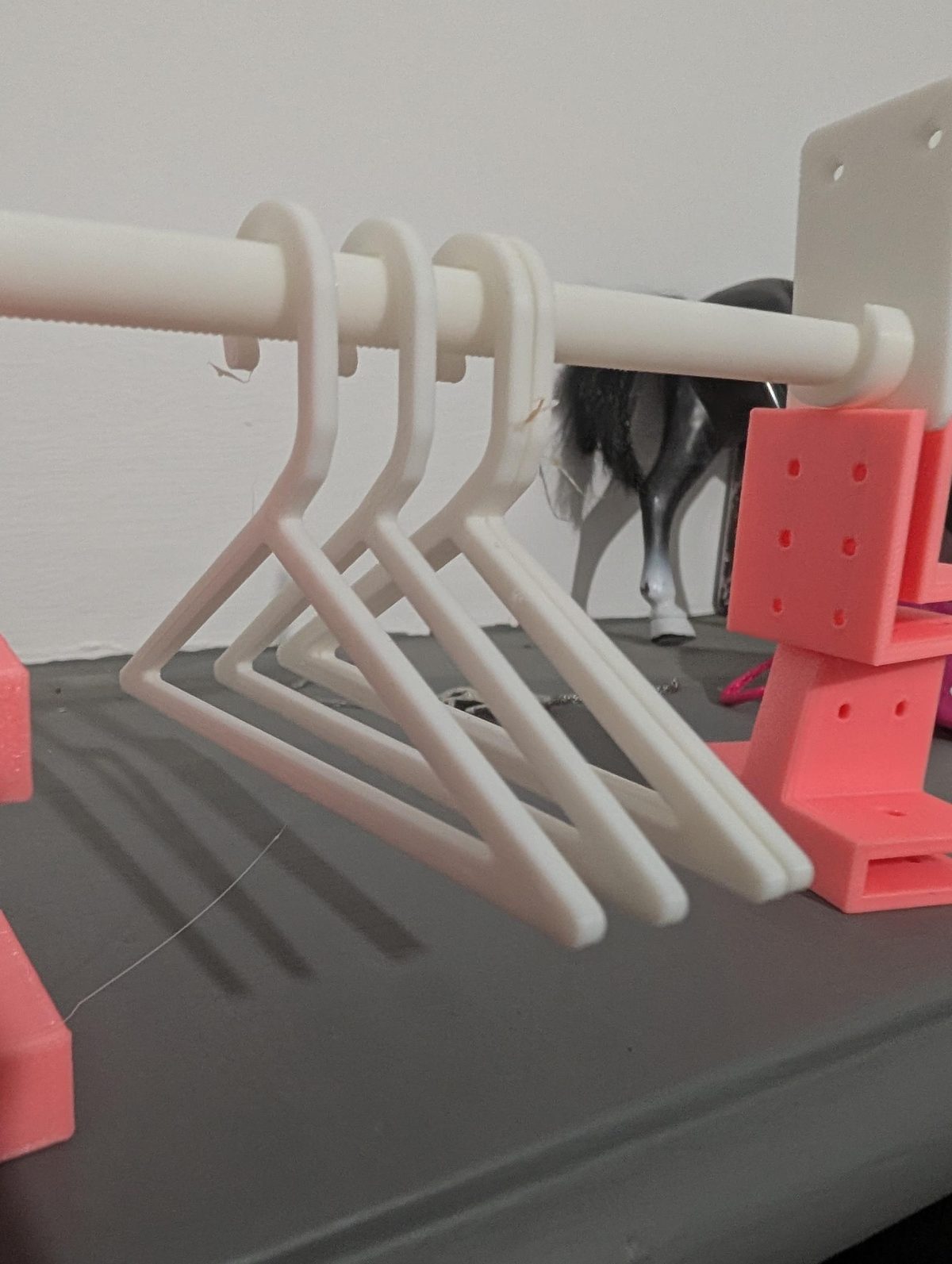 Three white hangers on the rail, their hooks curled over the pole and their bottom bars level.